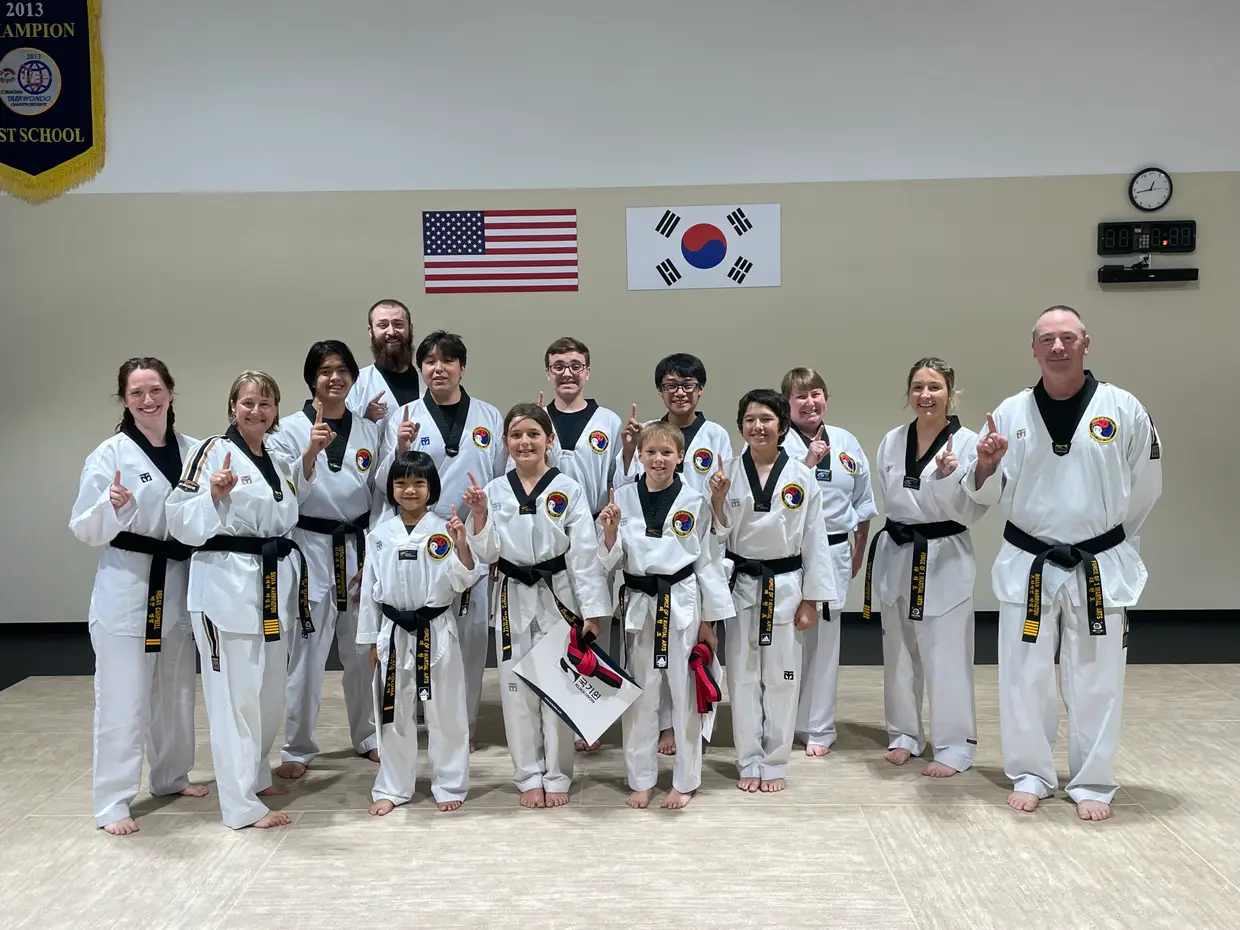 Force of One black belts of all ages standing together in the dojang beneath the American and Korean flags