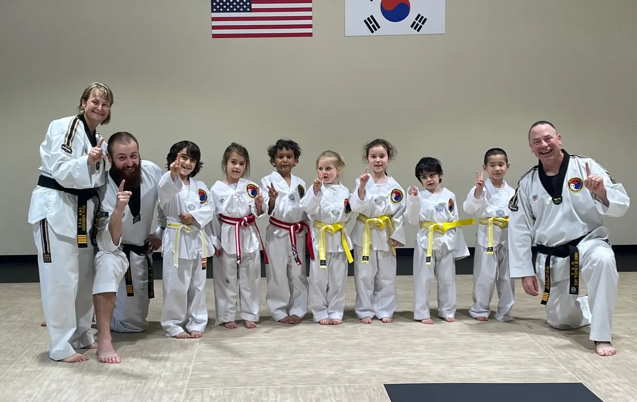 Young Force of One students lined up in white dobok with their instructors, under the American and Korean flags